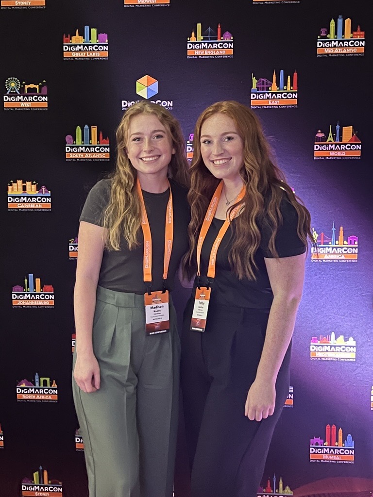 Two conference attendees standing in front of a DigiMarCon backdrop